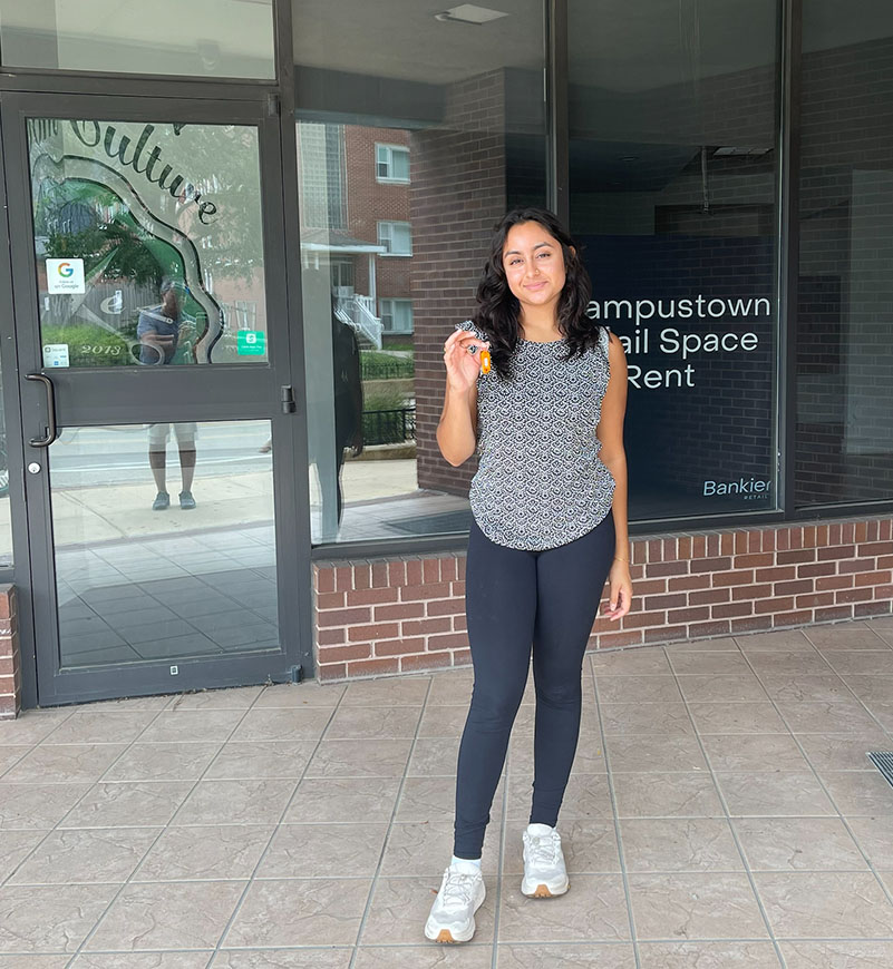 Vidhi standing in front of an empty storefront holding the key to the store.