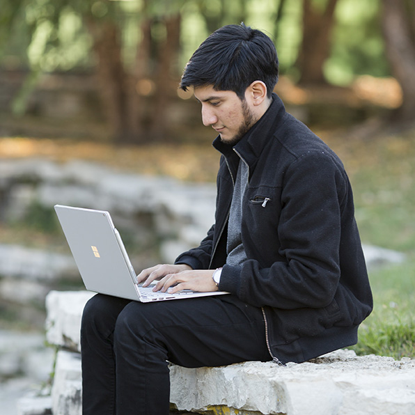 male student sitting outside with a laptop on his lap