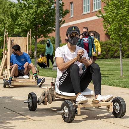 male student riding a handmade wooden vehicle