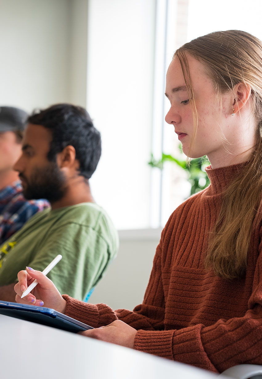 student writing on a tablet in class