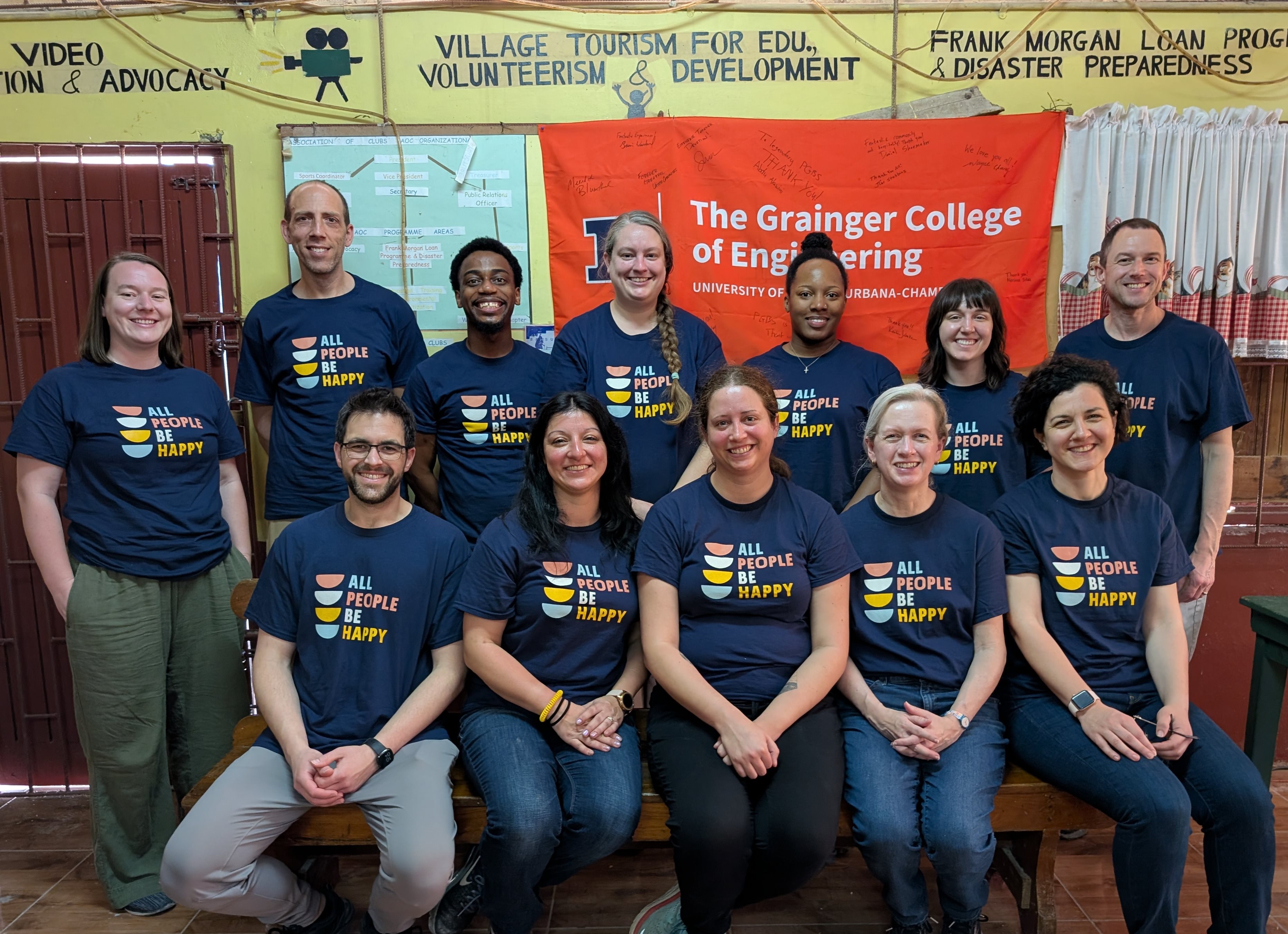 group of 12 engineering faculty sitting and standing in matching shirts, smiling at the camera. Grainger College of Engineering flag is behind them.