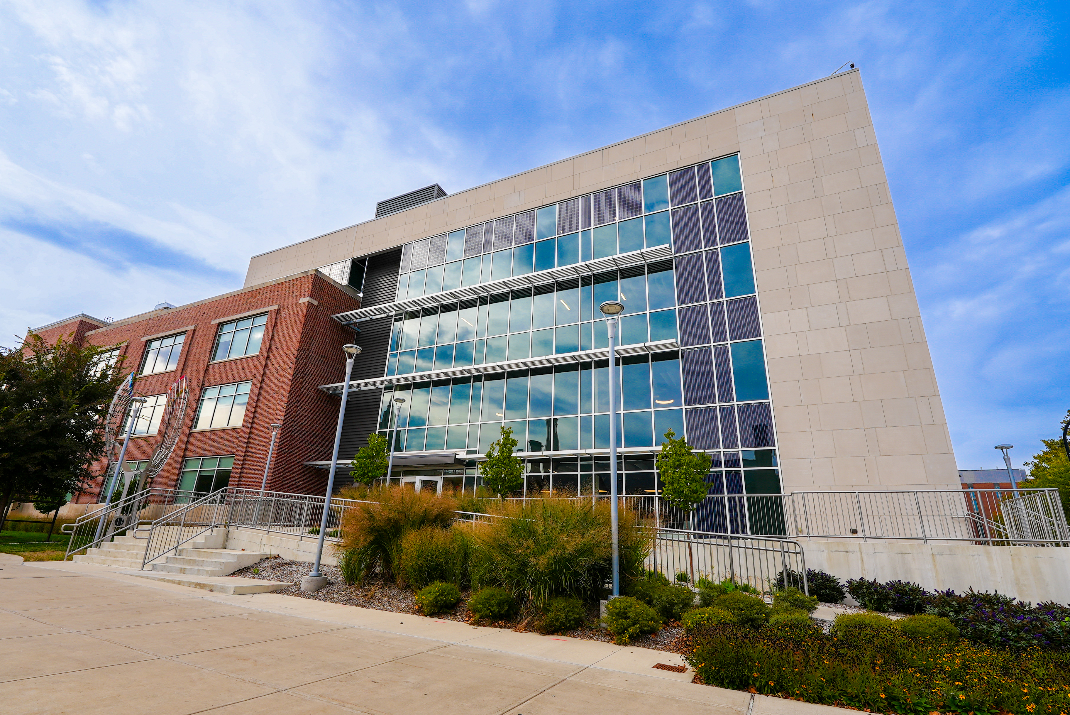 southeast corner view of the Sidney Lu Mechanical Engineering Building, showing a mostly glass atrium and limestone. Many native plants landscape the front of the building along Green Street.