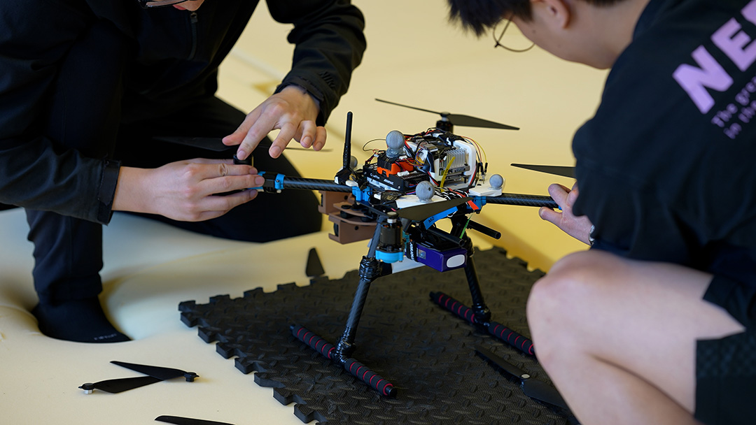 Students crouched down working on a drone.