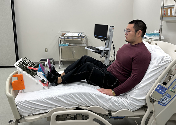 Male student in hospital bed pedaling the PedalPro with his feet
