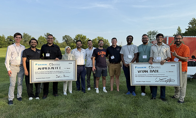 row of students standing outside, with two of them holding oversized winning checks