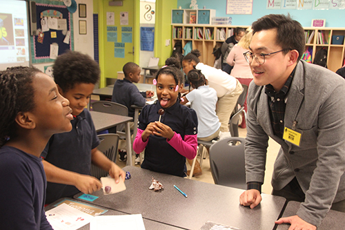 Jiho Kim interacts with BTW fourth graders as the students rub their suckers on sandpaper and lick them as part of a corrosive wear activity. (Photo by Joe Muskin)