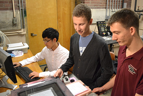 Grad student Tung-Wei Lin analyzes data on the computer, while undergrad Alex Kaczkowski and grad student Logan Rowe investigate a silicon wafer in Professor Harley Johnson's lab.