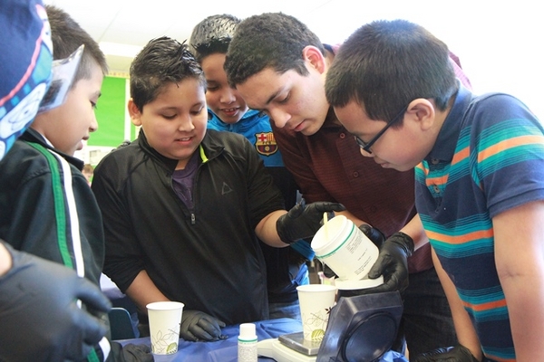 MechSE student Jesus Sotelo helps the fifth-graders measure PDMS for their bouncy balls.