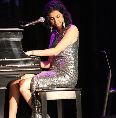 Anjali Ray wearing a sparkly dress playing a grand piano.