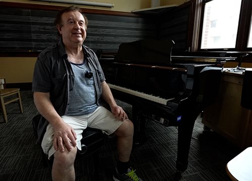 Joseph Bentsman sitting at a grand piano smiling at the camera.