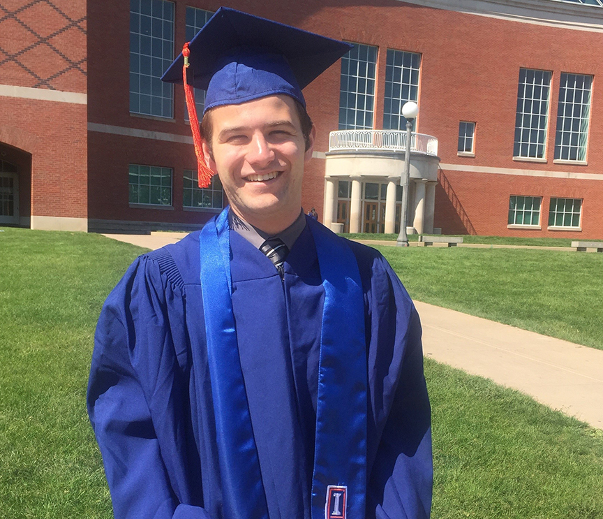 Mirabelli in a graduation cap and gown in front of Grainger Library.