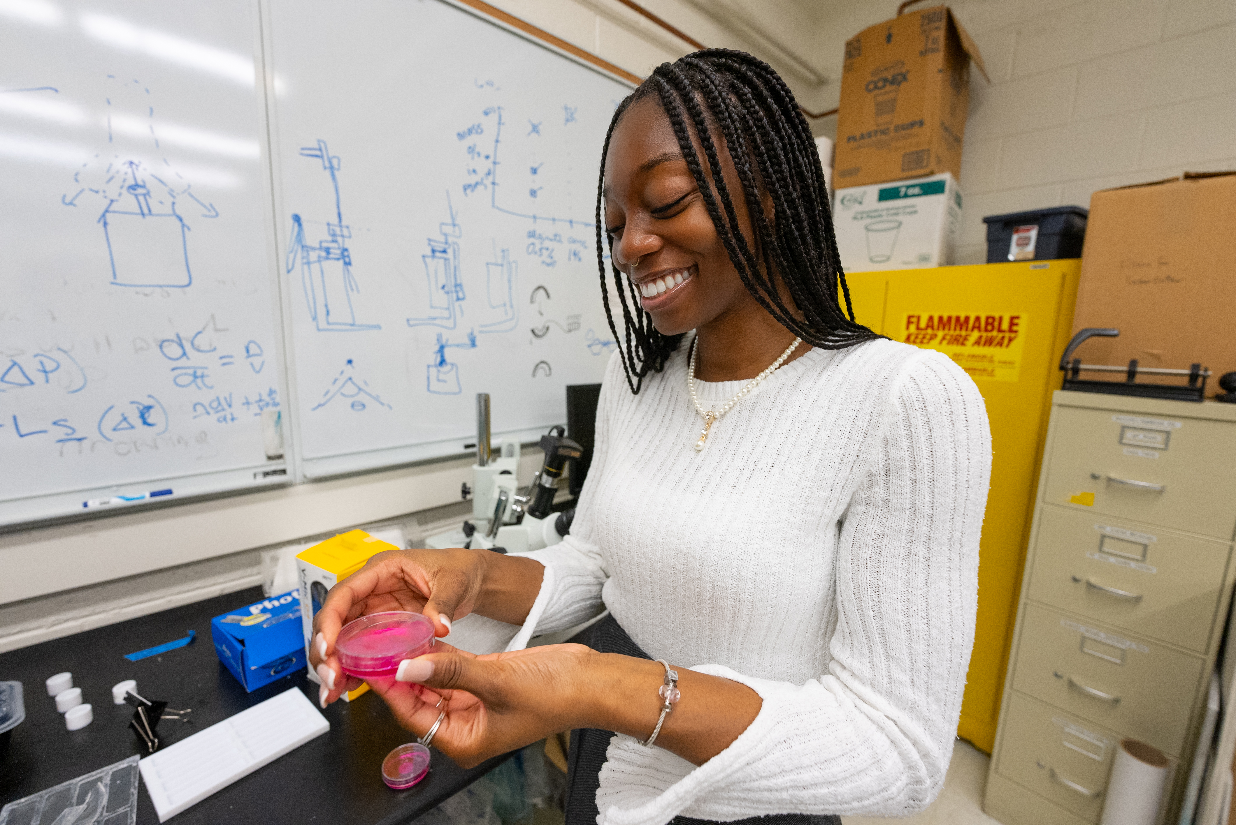 woman student holding petri dish with pink substance, in a lab.