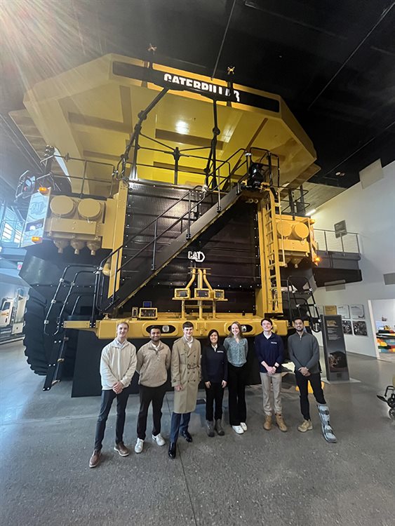 group of students standing in front of a huge Caterpillar machine